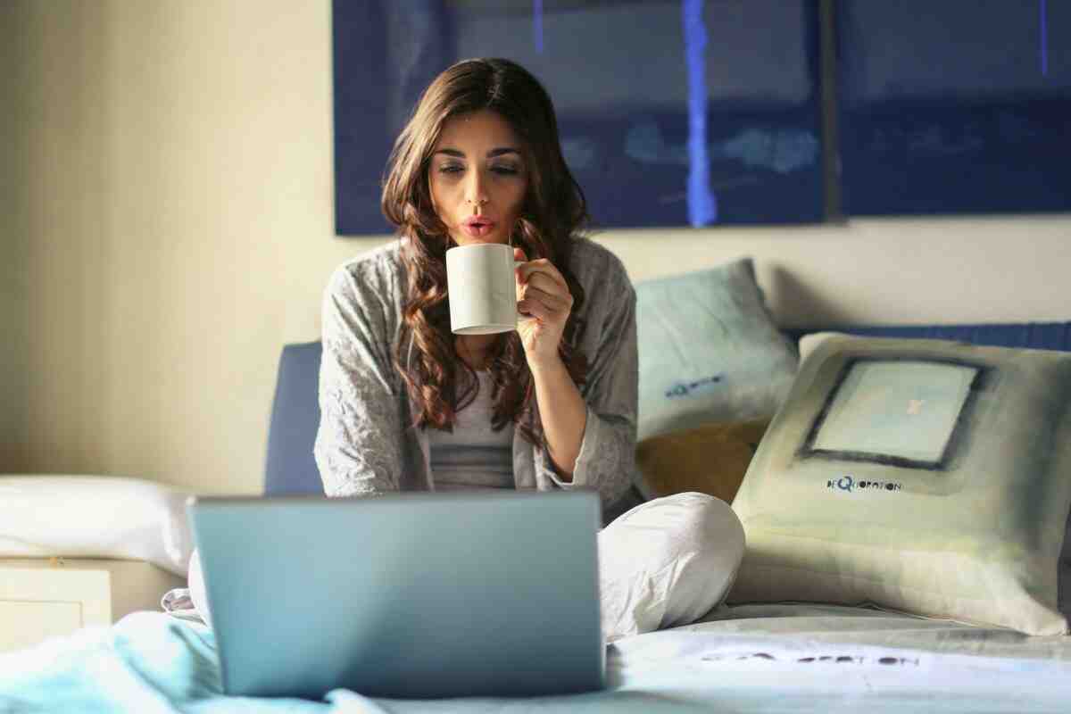woman-in-grey-jacket sits on bed uses grey laptop
