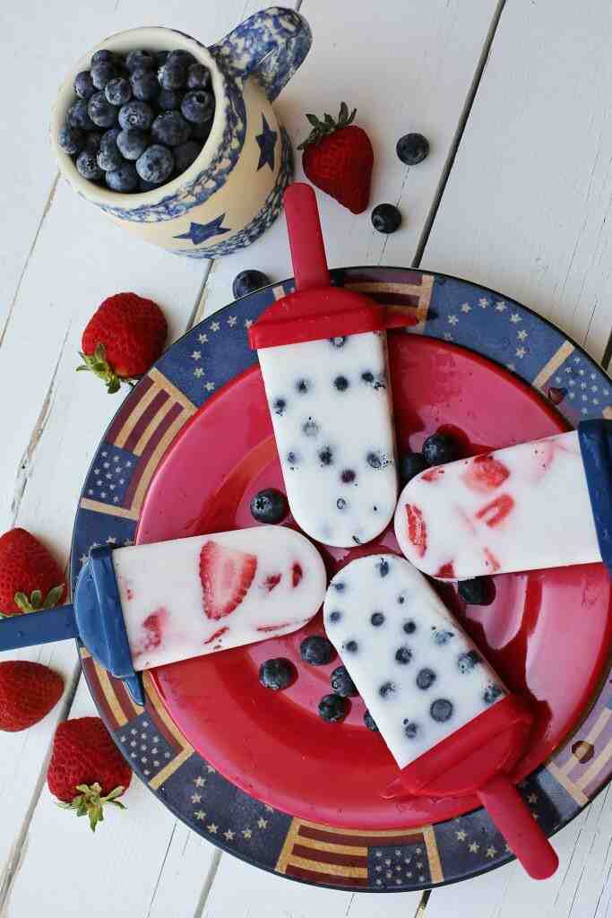 4 Fruit Popsicles with yogurt, blueberries and straberries on a red plate.