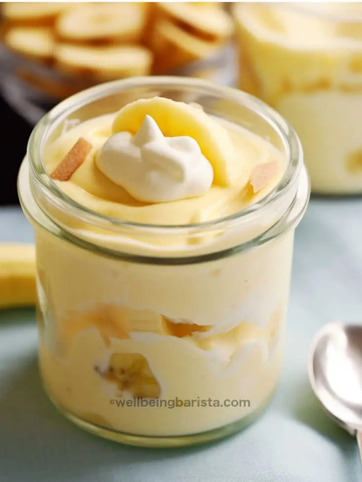 A small jar with healthy banana pudding with greek yogurt with some banana pieces in middle and top layer and a little yogurt on top as decoration