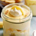 A small jar with healthy banana pudding with greek yogurt with some banana pieces in middle and top layer and a little yogurt on top as decoration