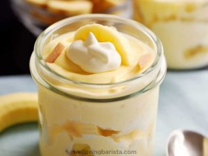 A small jar with healthy banana pudding with greek yogurt with some banana pieces in middle and top layer and a little yogurt on top as decoration