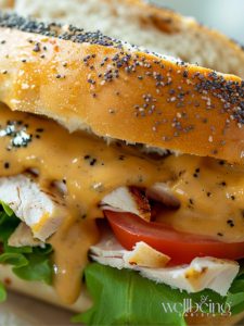 homemade sweet onion sauce, glossy and golden, drizzling over a fresh Subway-style sandwich. The sauce has a smooth, velvety texture with tiny specks of onion flakes and poppy seeds. Shot on a marble countertop with natural lighting, fresh lettuce, tomatoes, and turkey visible in the sandwich.