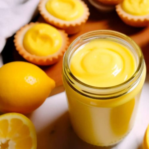 lemon curd sauce in a jar with portuguese tarts filled with lemon curd.