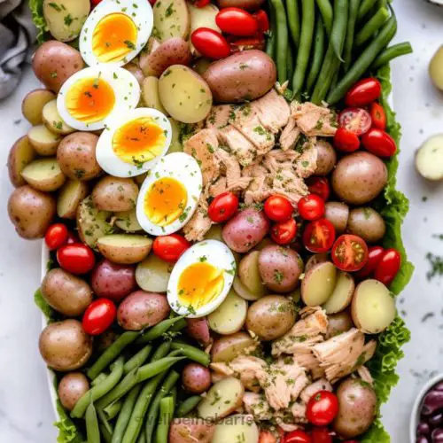 A big platter of Salad Nicoise with green beans, halved potatoes, cherry tomatoes, hard boiled eggs, black olives and anchovy fillets