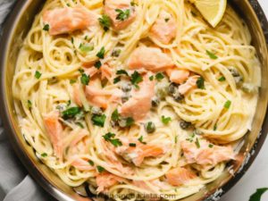 a pan with smoked salmon linguine with capers and parsley, chives and lemon to garnish.