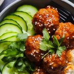 gochujan turkey meatballs with sesame on top served on a bed of rice and sliced cucumbers