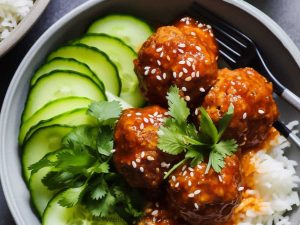 gochujan turkey meatballs with sesame on top served on a bed of rice and sliced cucumbers