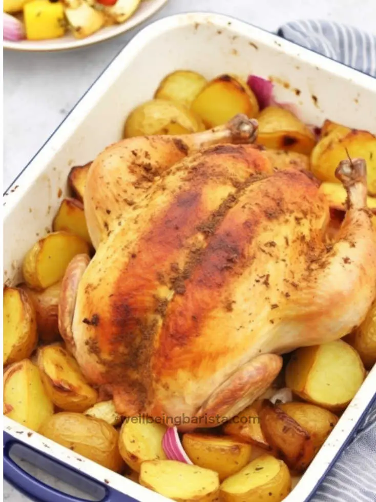 A roasted whole chicken with drippings, quartered onions and roast potatoes in one dish.