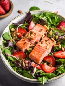 grilled salmon summer salad with strawberries on a bed of green salad